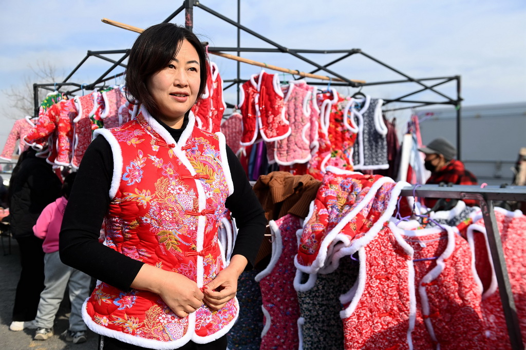 12月29日，在山东青岛西海岸新区泊里大集，一名消费者在试穿新年喜庆服装。新华社发（俞方平摄）