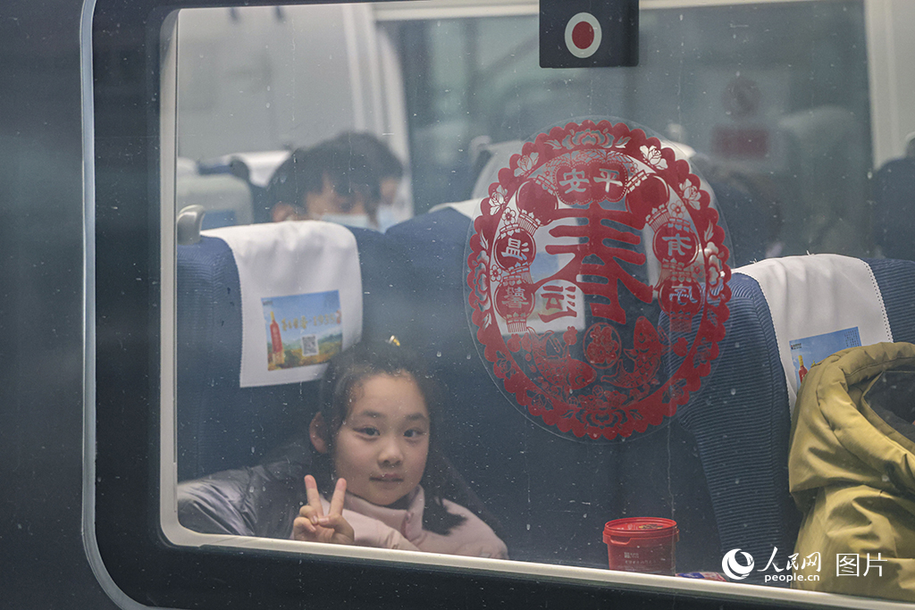 2025年春运首日，上海虹桥火车站，一位小旅客坐在即将开行的列车上，隔着玻璃窗对镜头比耶。人民网记者 王初摄
