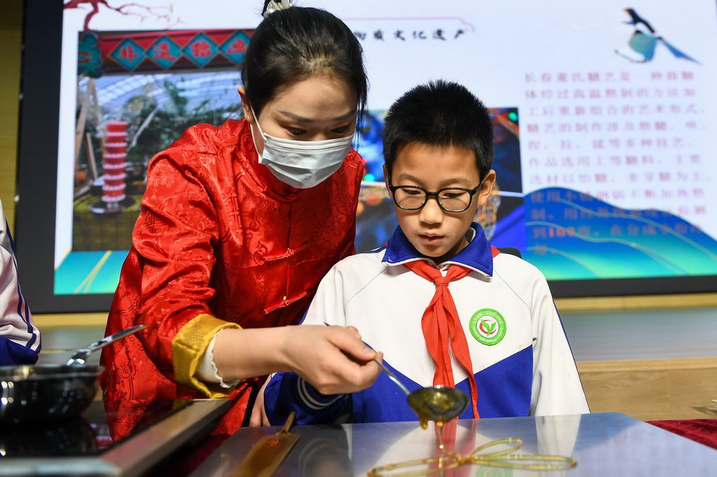 2月24日，在吉林省第二实验朝阳学校，糖画艺人董露露（左）指导学生制作糖画。