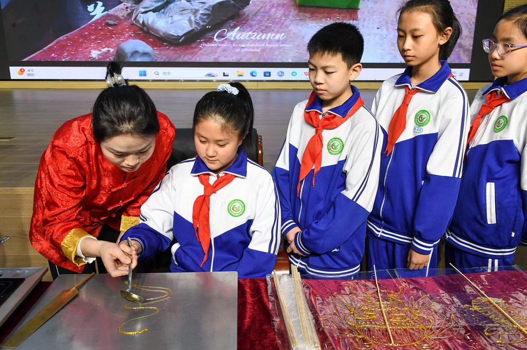 2月24日，在吉林省第二实验朝阳学校，糖画艺人董露露（左一）指导学生制作糖画。