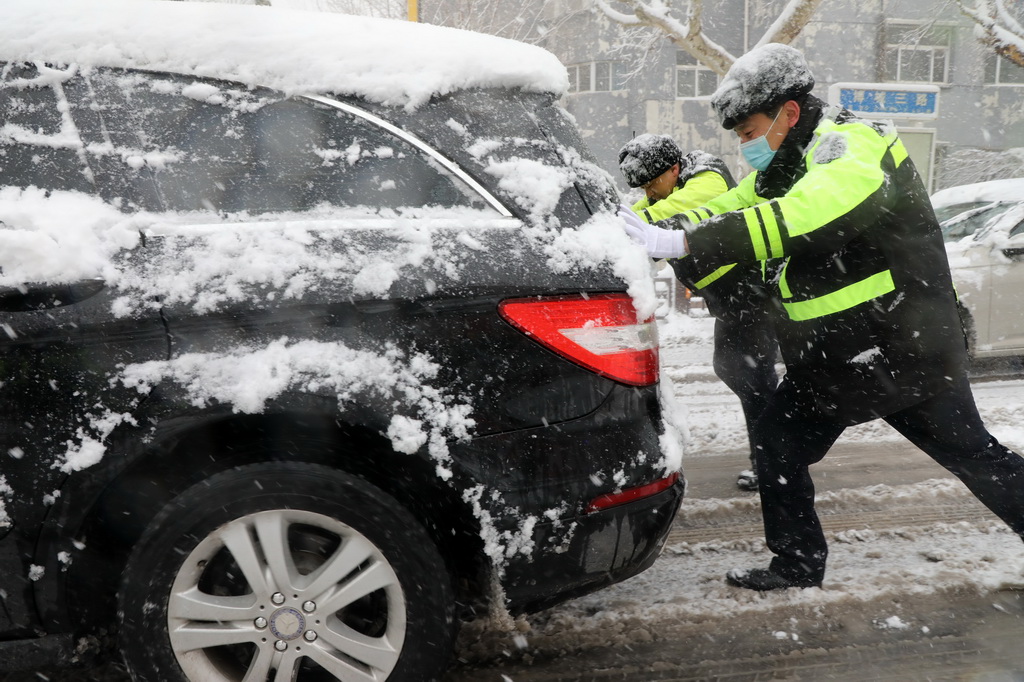 3月2日，在山东省滨州市博兴县城区街头，执勤交警在雪中帮助市民推车。新华社发（陈彬摄）