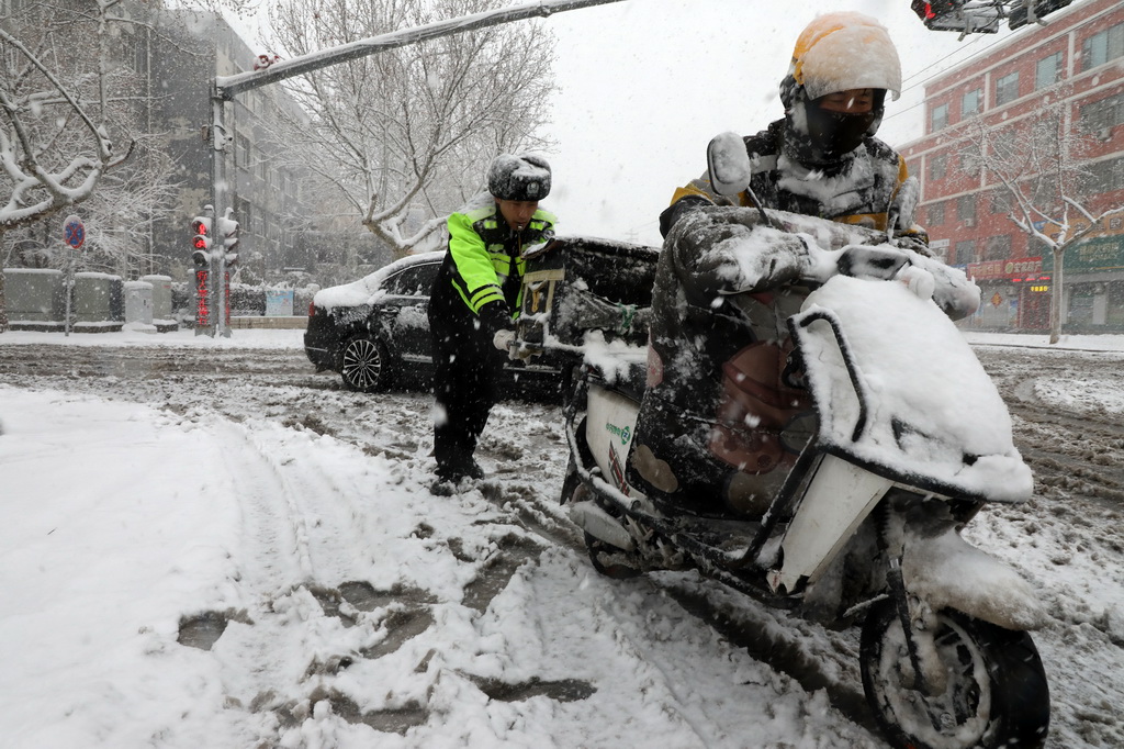 3月2日，在山东省滨州市博兴县城区街头，执勤交警在雪中帮助一外卖小哥推电瓶车。新华社发（陈彬摄）
