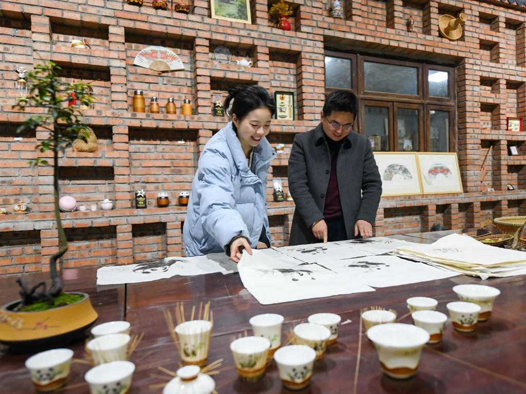 在崇州市朱利原乡非遗文化园，白静波和女儿白梓忆在查看“熊猫抱竹”设计草图（3月7日摄）。新华社记者 王曦 摄