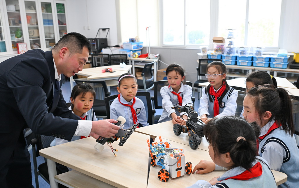 3月27日，重庆市江北区新村同创小学科创社团指导老师（左一）向学生讲解自动化设备运行原理。
