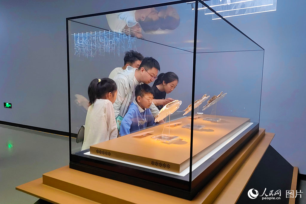 2025年5月3日，河南安阳殷墟博物馆内，游客驻足在甲骨文展区。3000年前的龟甲历经岁月打磨，仍清晰可见苍劲的刻痕，游客透过这些承载着文明密码的古老文字，仿佛能看到祭祀的盛大场景，真切触摸到华夏文明传承的脉络，感受着中华文化穿越千年的强大生命力。人民网记者 单芳摄