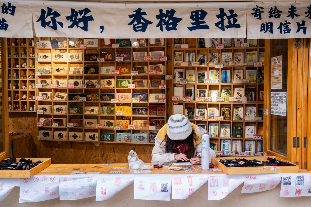 一名游客在云南省迪庆州香格里拉市独克宗古城写明信片（2025年3月7日摄）。