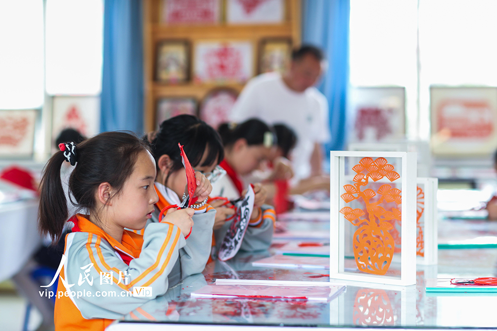 2025年5月17日，在陕西省旬邑县逸夫小学，学生在老师的指导下学习剪纸。