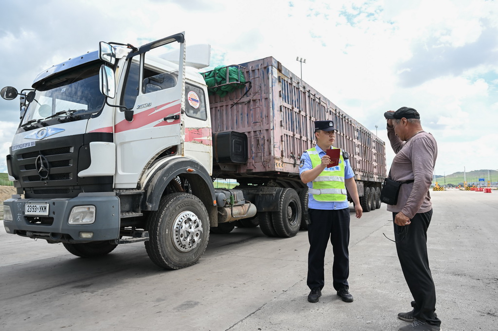 7月10日,在珠恩嘎达布其口岸,珠恩嘎达布其出入境边防检查站移民管理警察(左)查验货车司机证件。