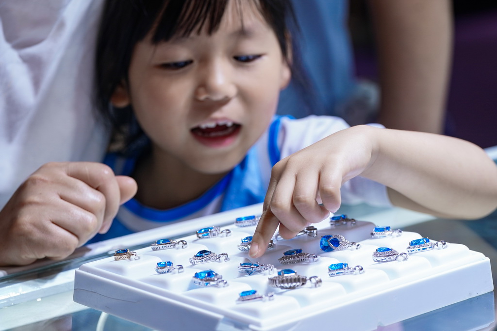 7月10日，小朋友在昆明石博会上帮家长挑选玉石。