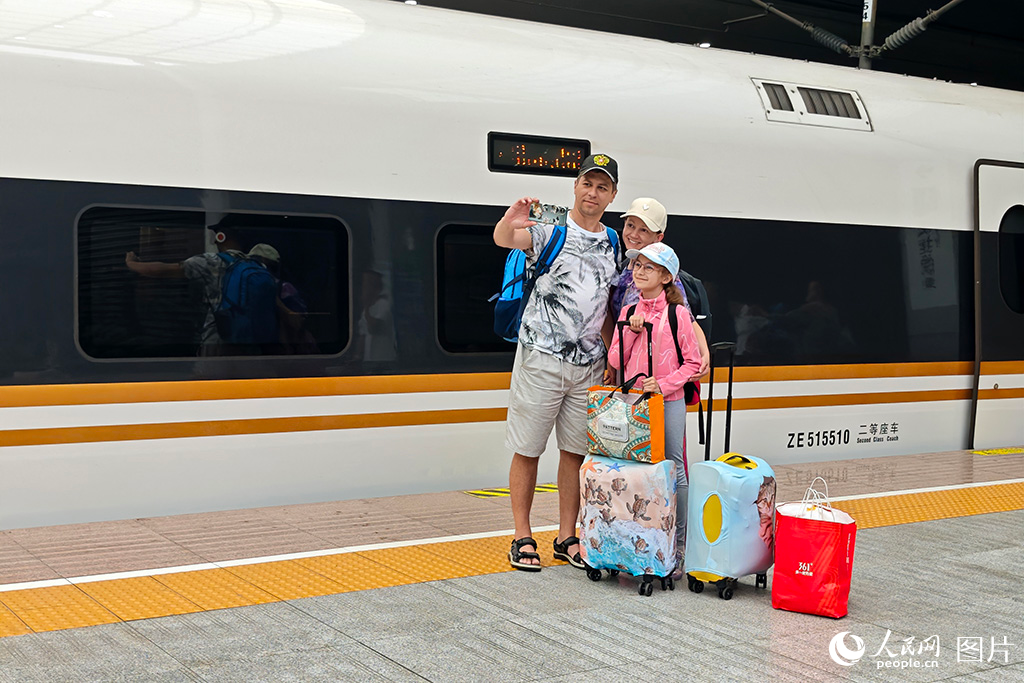 2025年6月23日，在上海站，外国游客下车后在高铁前合影留念。人民网记者 翁奇羽摄