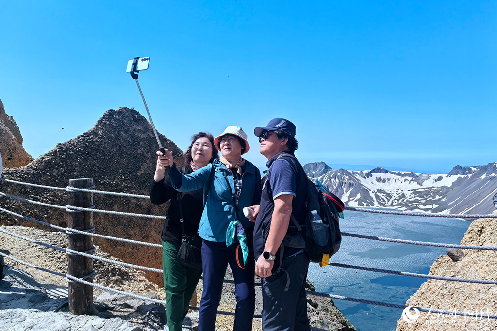 2025年6月14日，韩国游客举起手机和吉林长白山天池合影，记录下天池开冰的壮观景象。人民网记者 王海跃摄
