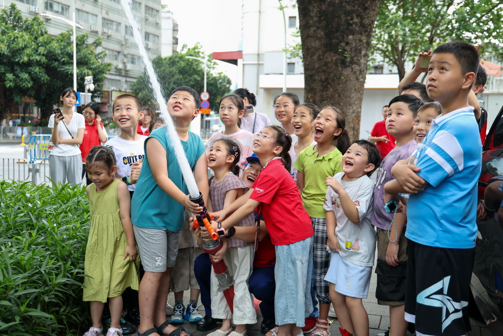 7月15日，小朋友在深圳市福田区梅丰小型消防站开放日活动中体验多功能消防水枪。