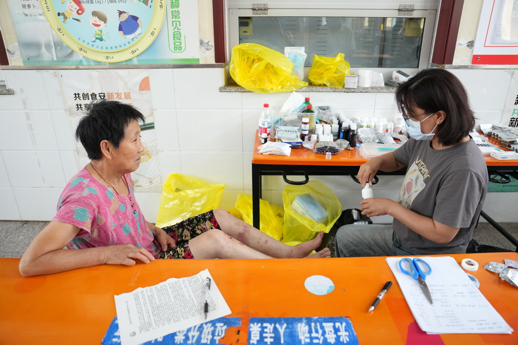 7月29日，在北京市密云区太师庄中学居民安置点，太师屯镇社区卫生服务中心的医生（右）为居民处理伤口。