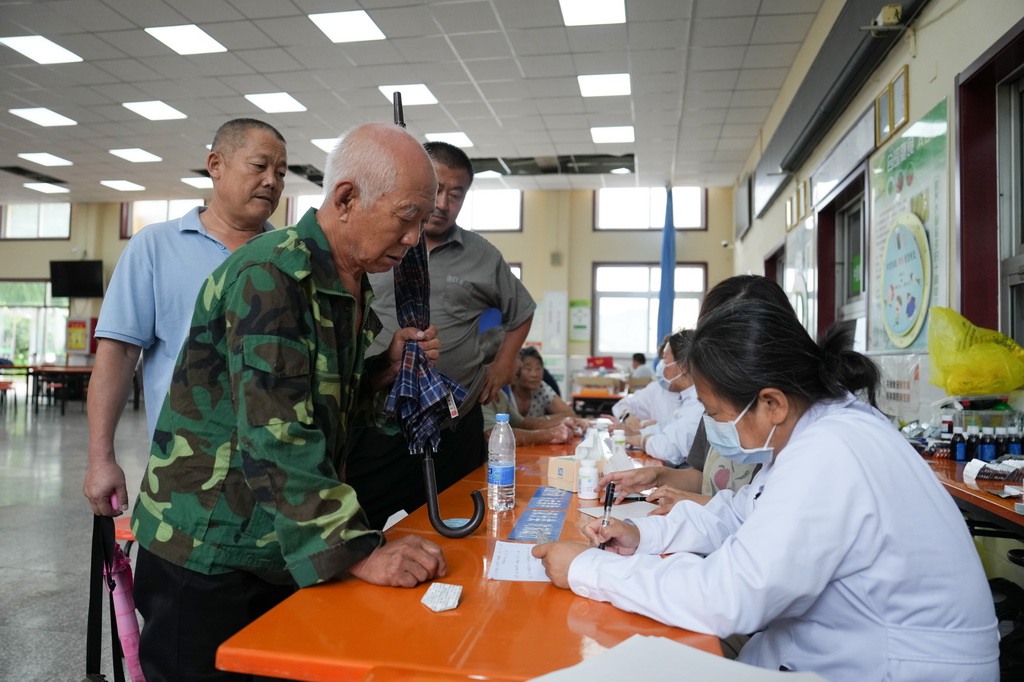 7月29日，在北京市密云区太师庄中学居民安置点，太师屯镇社区卫生服务中心的医生（右）为安置在此的群众开药。