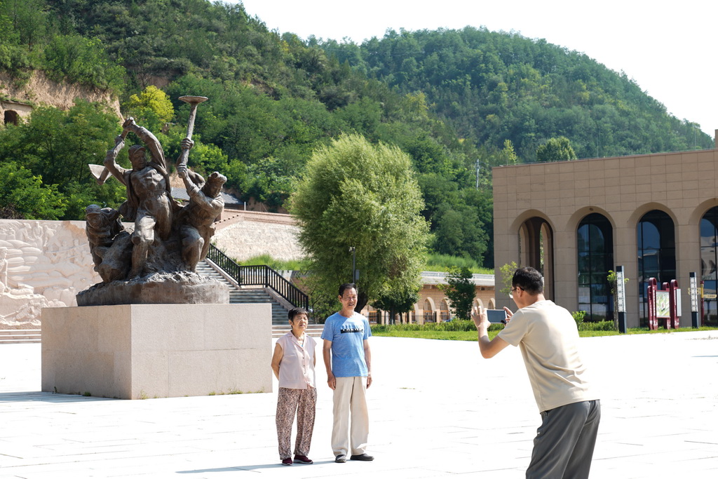 游客在南泥湾大生产纪念广场的雕塑前合影（7月29日摄）。