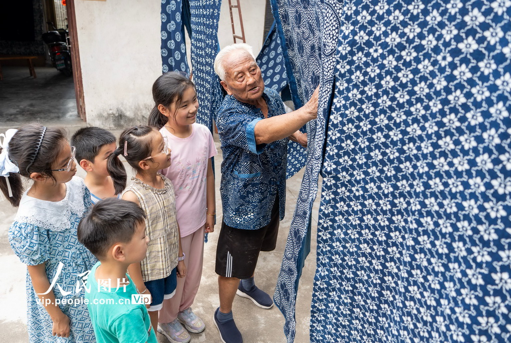 8月4日，国家级非遗南通蓝印花布印染技艺代表性传承人王振兴老人向小朋友介绍蓝印花布的制作技艺。