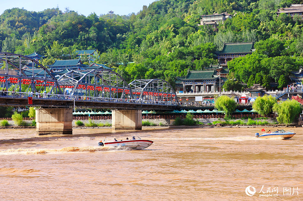 9月9日，黄河边，茶摊上飘着“三炮台”的玫瑰香气，百年铁桥红灯笼高悬，水鸟翩跹，游人沿河道悠然漫步。在兰州，黄河南北两岸山脉绵延，分别为北部山区和南部山区，俗称“南北两山”。近年来，甘肃省兰州市积极推动黄河流域生态保护与高质量发展，持续加强生态修复，绿色发展成效不断巩固。截至目前，南北两山绿化面积已达62万余亩，1.6亿多株苗木在黄河水的滋养下茁壮成长，形成了较为完善的人工林生态体系。该体系每年可减少泥沙淤积超过56万立方米，全市水土保持率提升至71%以上，生态效益显著。人民网记者 焦隆摄