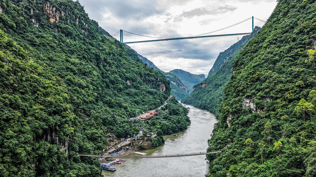 景区内的索道桥与远处的花江峡谷大桥遥相呼应（9月27日摄，无人机照片）。