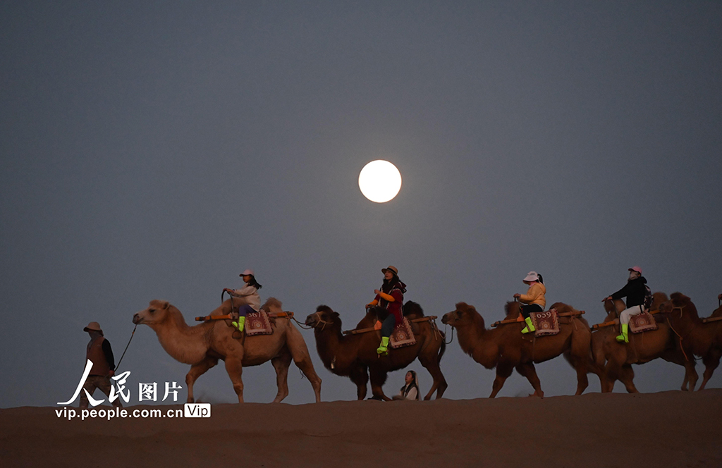 10月6日晚，游客在甘肃省敦煌市鸣沙山月牙泉景区骑骆驼赏明月。张晓亮摄（人民图片网）