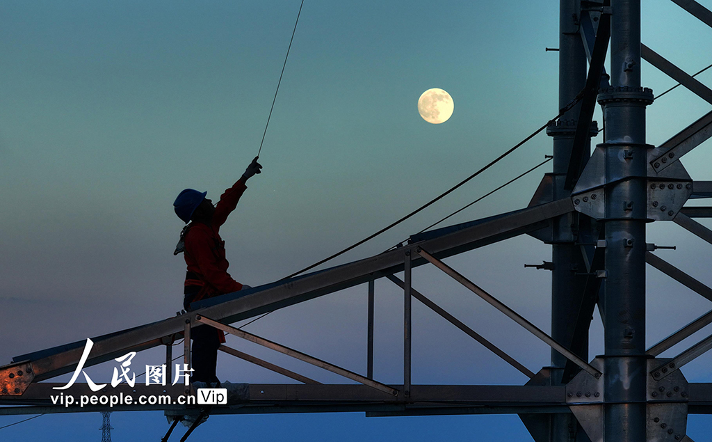10月6日，在湖南省衡阳市雁峰区南三环路上，施工人员在高塔进行架线施工作业时与圆月同框。曹正平摄（人民图片网）