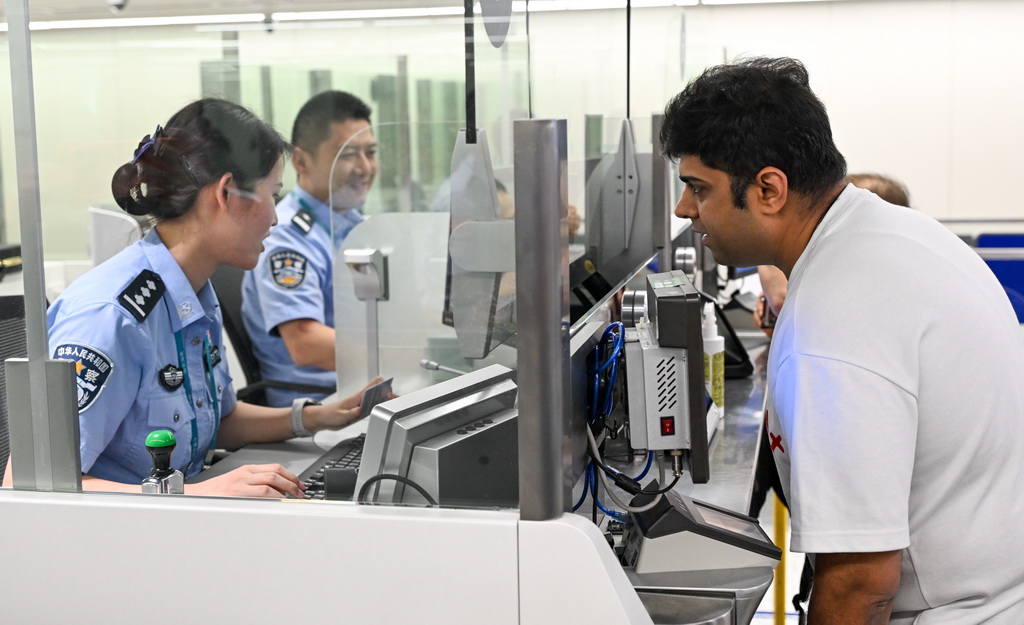 10月15日，在海口美兰边检站，海南2025年第200万名通关外籍旅客卡迪克（右）在办理边检手续。