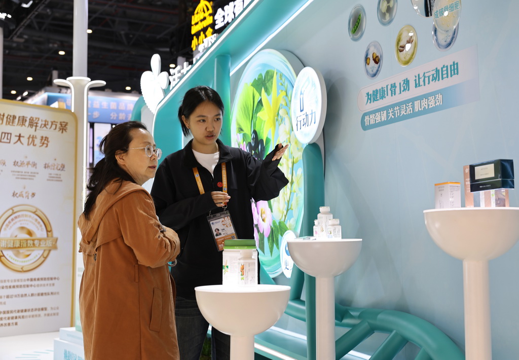 11月8日,在第八届进博会消费品展区,参观者(左)听工作人员介绍健康保健产品。新华社记者 方喆 摄