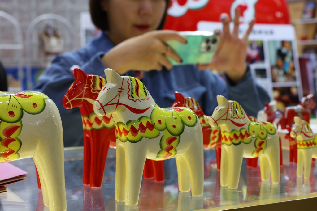 11月7日,在第八届进博会消费品展区,参观者在拍摄一组瑞典传统手工艺达拉木马展品。新华社记者 方喆 摄