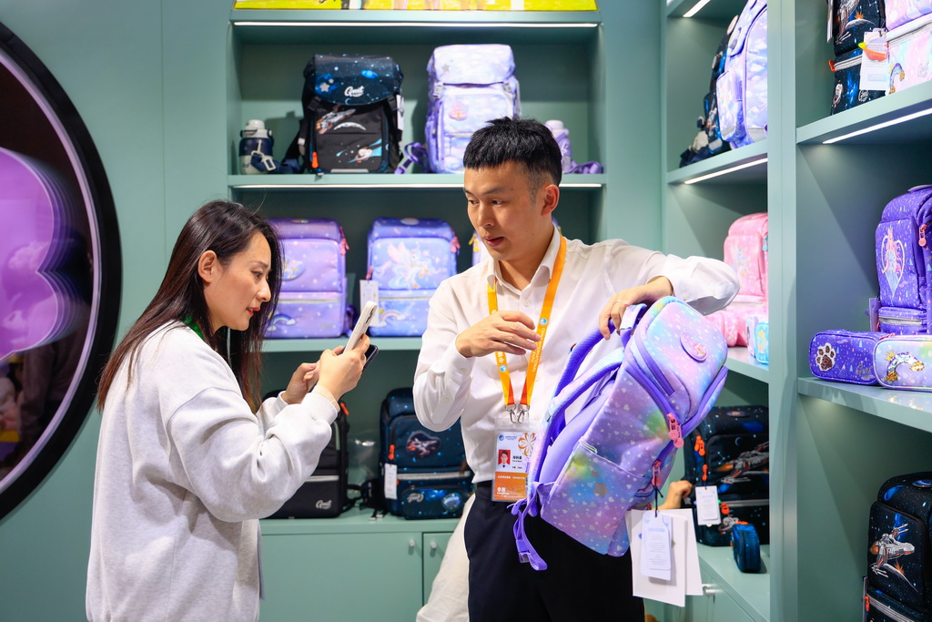 11月8日,在第八届进博会消费品展区,观众(左)在一家儿童书包品牌展台咨询产品。新华社记者 刘佳琪 摄