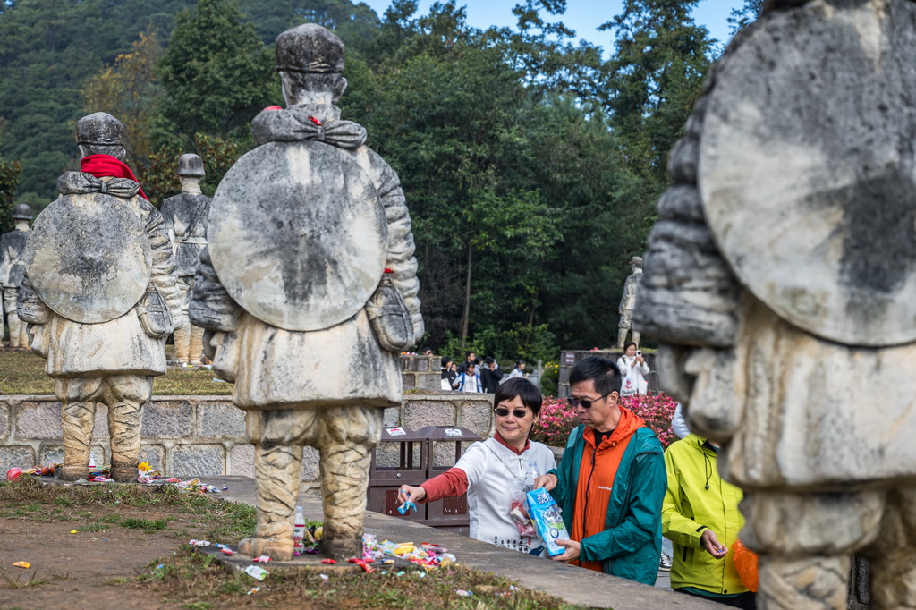 11月20日，游客在云南省保山市龙陵县松山战役旧址参观时向娃娃兵雕像敬献糖果。