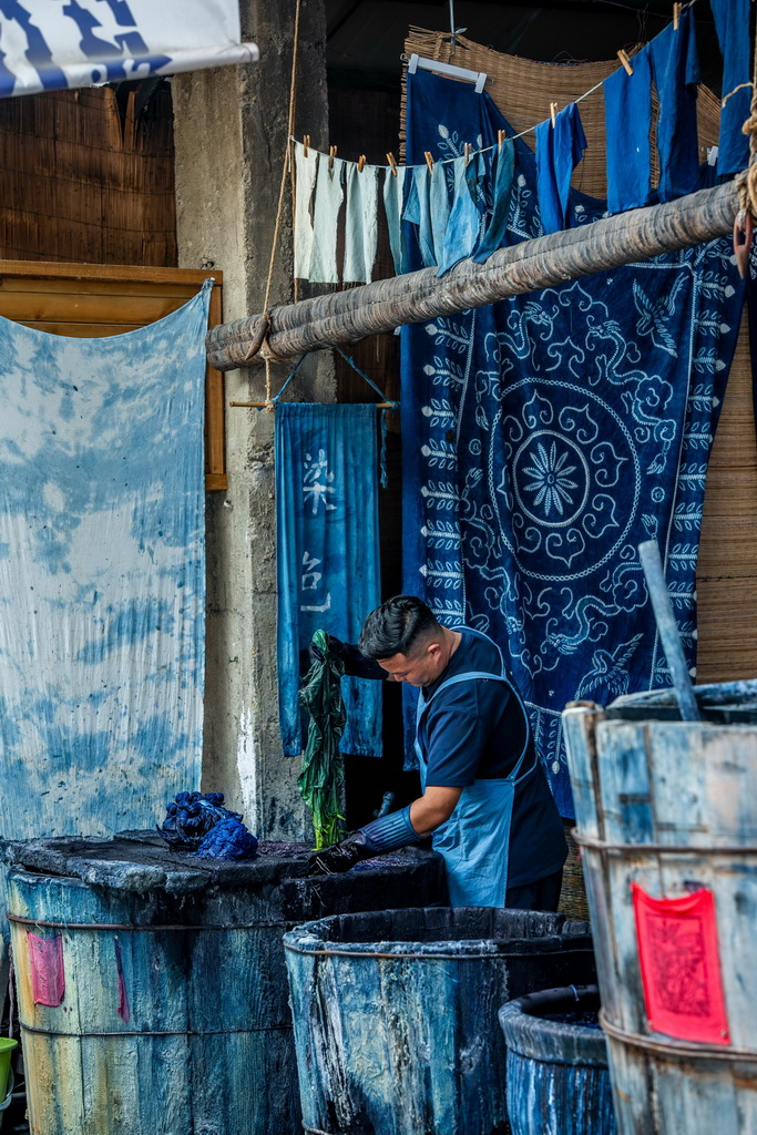 白族扎染技艺传承人段袁在周城村“璞真染坊”将缝扎好的布料放入染缸内浸染(11月21日摄)。