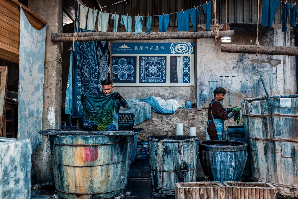 白族扎染技艺传承人段袁（左）在周城村“璞真染坊”将缝扎好的布料放入染缸内浸染（11月21日摄）。