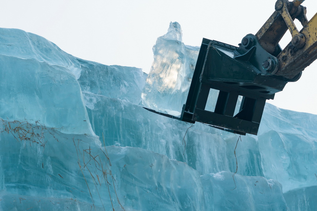 11月24日,在哈尔滨冰雪大世界存冰场,工程车辆从冰垛上取冰。