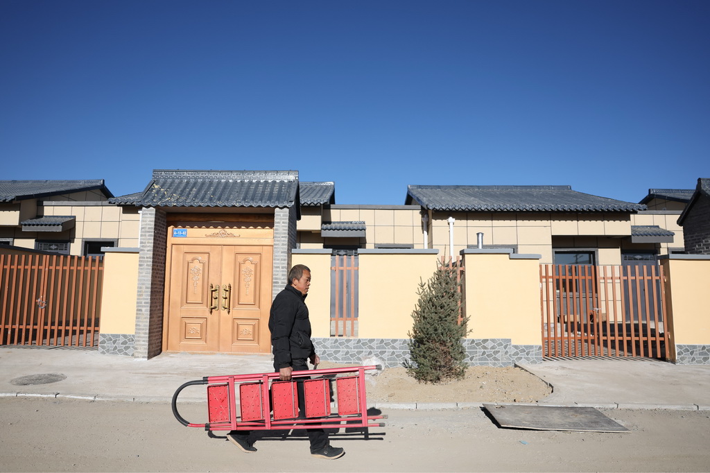 12月1日，在榆中县马坡乡旧庄沟村安置点，村民王利军提着梯子从新家门前的路上走过。
