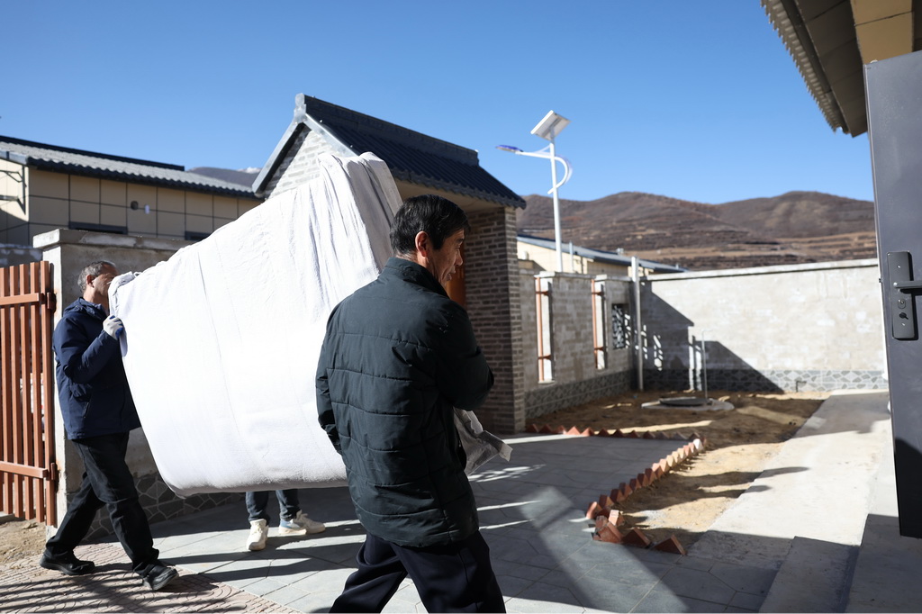 12月1日,在榆中县马坡乡旧庄沟村安置点,两名工人将床垫搬入受灾群众的新居。