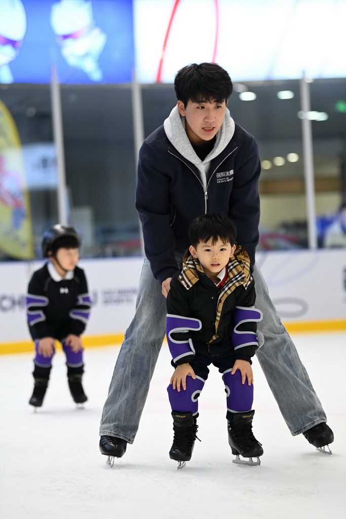 12月3日，教练马帅（上）在冰上运动公益课上指导初学滑冰的小学员。