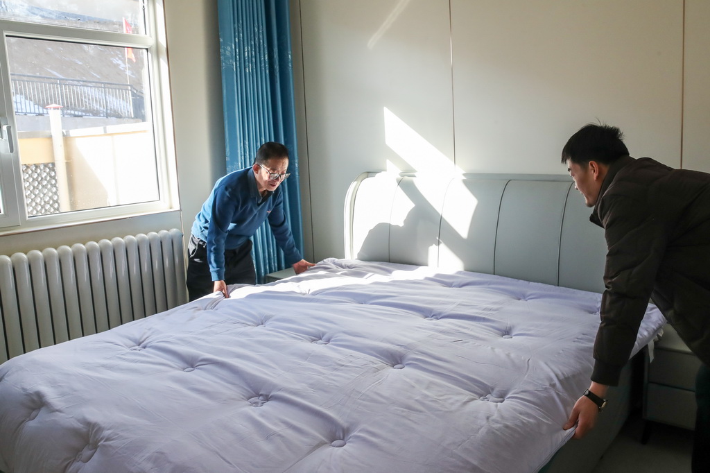 12月29日，村民张伦贤（右）在榆中县马坡乡马莲滩村集中安置点的新家里整理床铺。