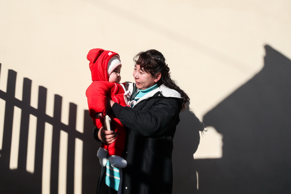 12月29日，村民抱着孙子在榆中县马坡乡马莲滩村集中安置点的新家晒太阳。