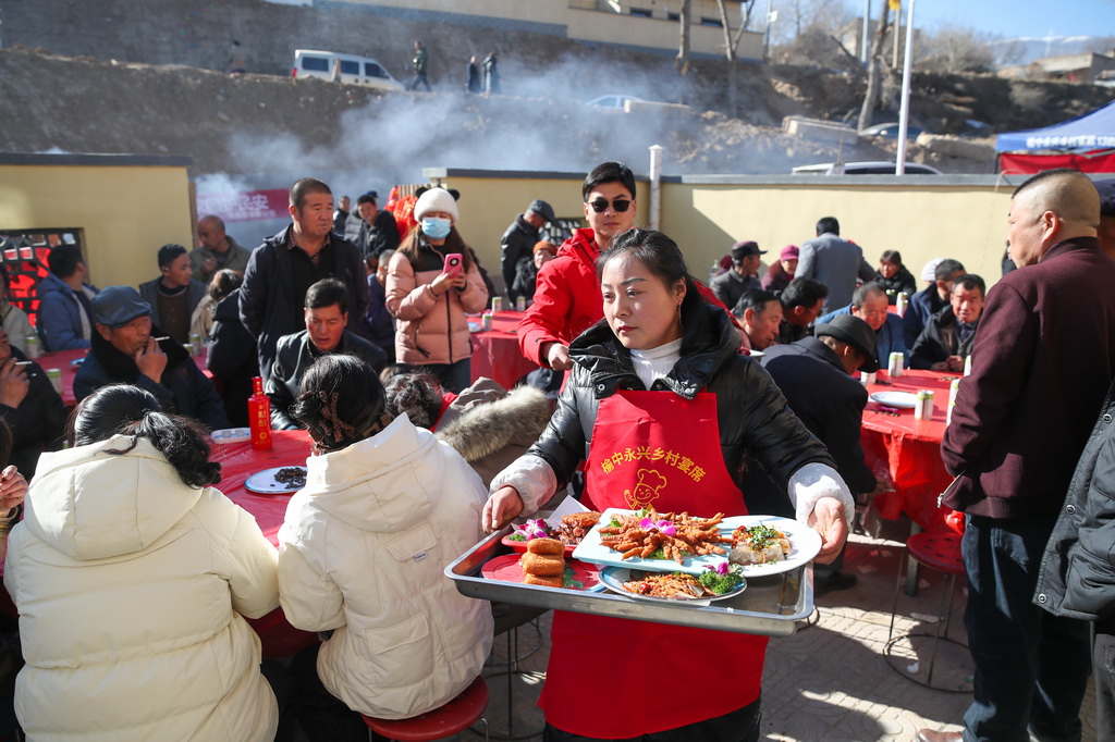 12月29日，帮厨人员在榆中县马坡乡马莲滩村集中安置点的乔迁宴上端菜。