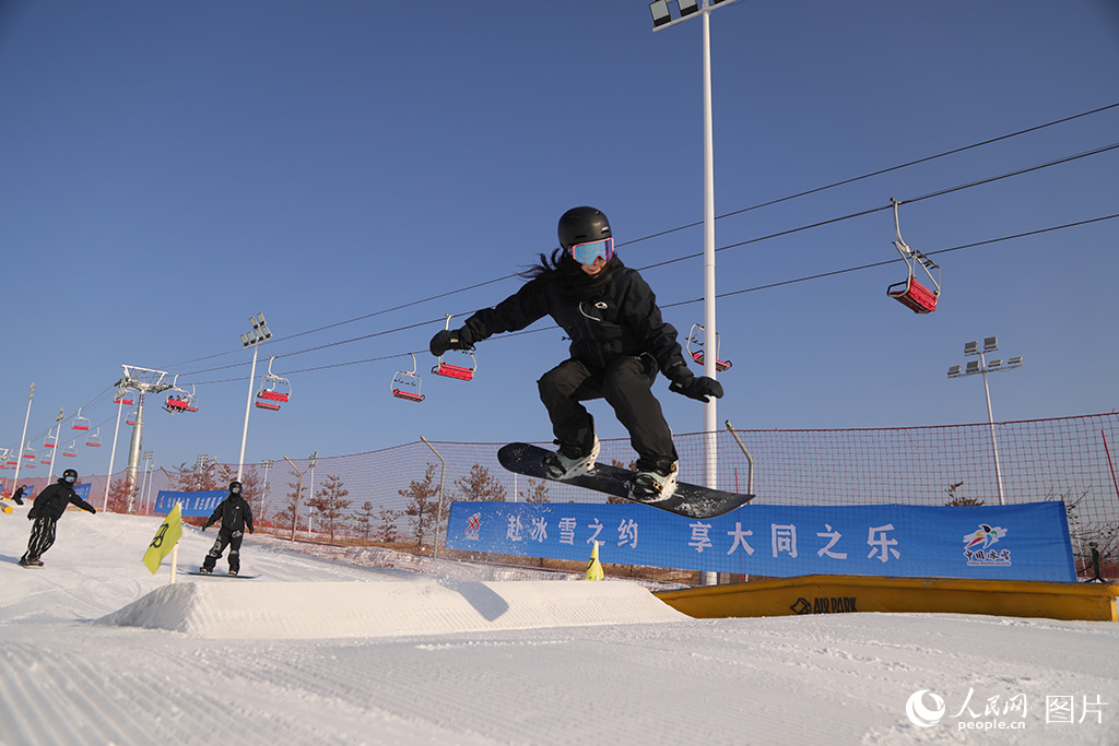 2026年1月11日，在山西省大同市万龙白登山国际滑雪场，滑雪运动爱好者们展示独特技巧，享受冰雪。2025—2026大同冰雪季以“游古都 嬉冰雪 强体魄 品美食”为核心主题，融合19项滑冰、滑雪、冰钓等系列赛事活动。此外，2025年山西省冰雪消费券发放活动将持续至2026年3月，共计投入200万元冰雪消费优惠补贴，惠及山西冰雪爱好者，精准释放冰雪消费潜力。人民网记者 王帆摄