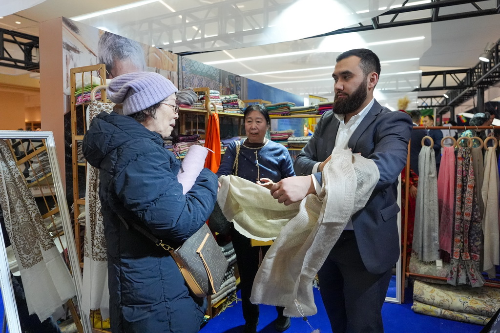 2月4日，在“共享大市场·出口中国”2026年首场活动暨北京国际精品荟的进口商品推介区，参观者（左）购买展出的乌兹别克斯坦围巾。