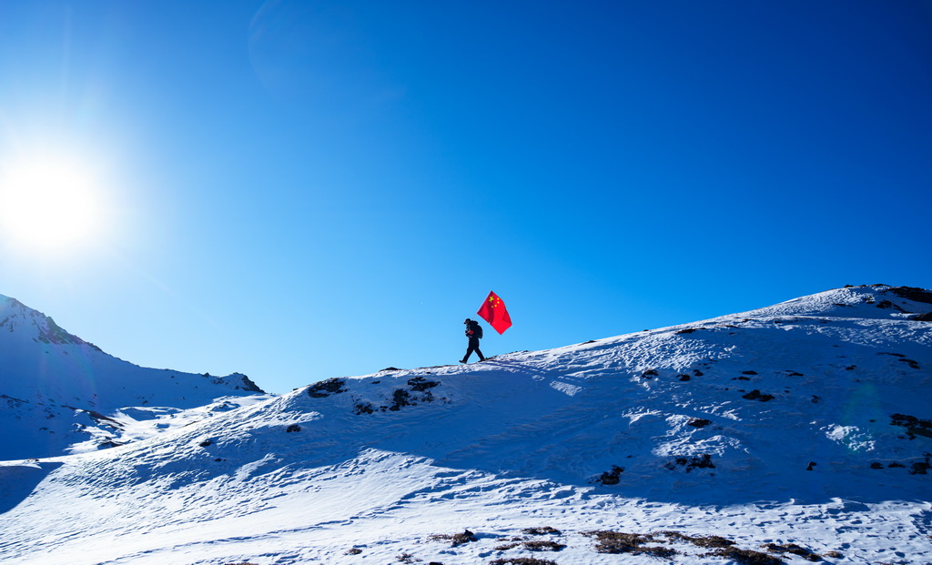 在西藏山南市隆子县玉麦乡境内,护边员普布罗布扛着国旗行走在雪坡上(2月6日摄)。