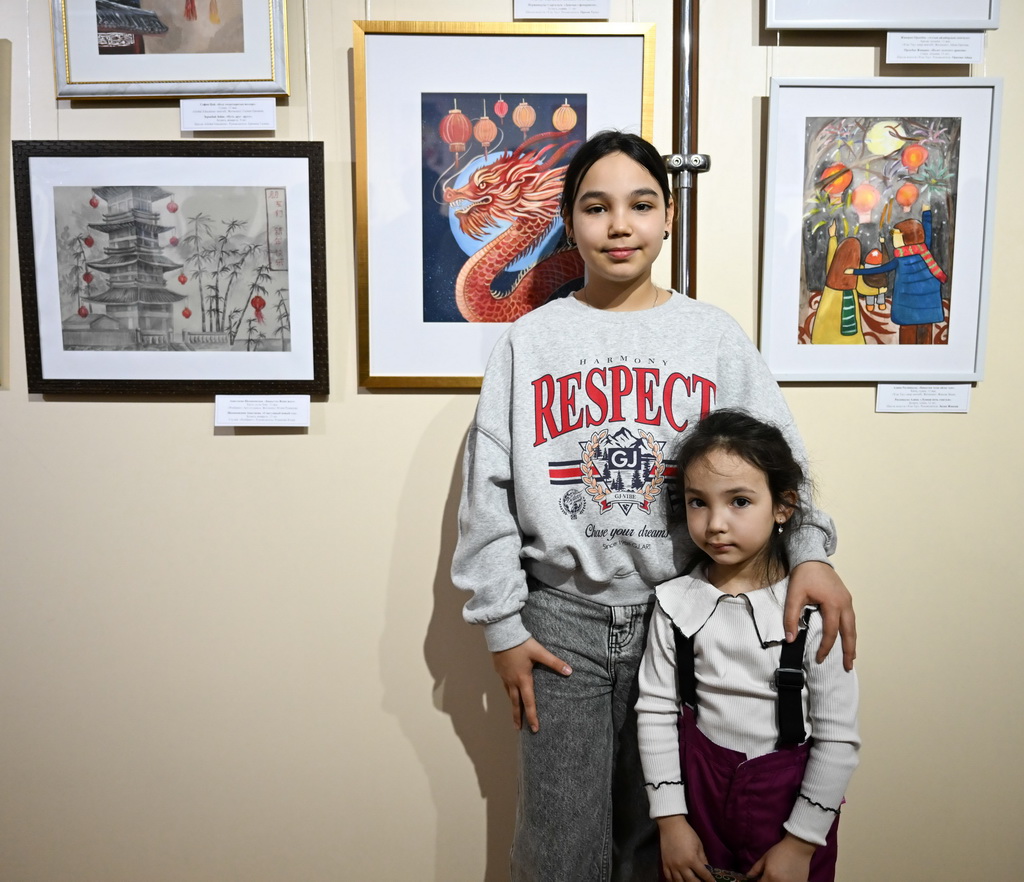 2月23日,在位于阿拉木图的哈萨克斯坦中央国家博物馆,一名学生(左)在自己的作品前拍照留念。