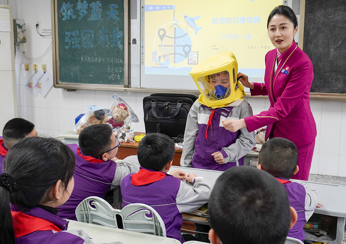 3月5日,在重庆市九龙坡区谢家湾朵力小学校的课堂上,来自重庆航空的空乘人员和学生一起演示如何正确使用客机上的应急处置装备。