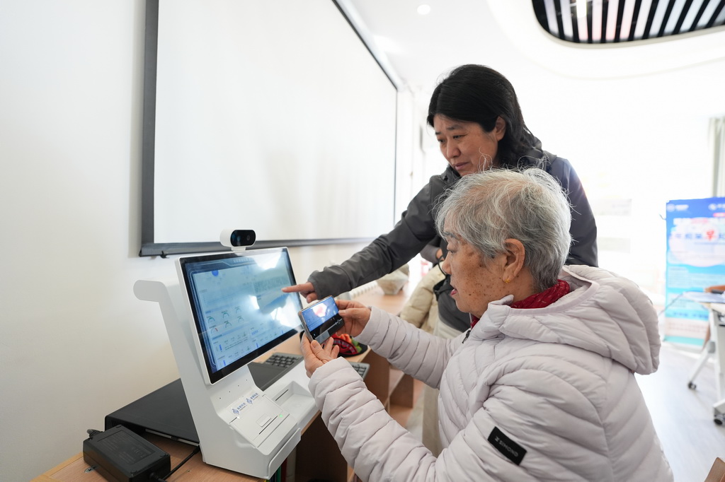 一名社区居民（前）在智慧康养机器人养老驿站内体验一款智慧健康设备（3月18日摄）。