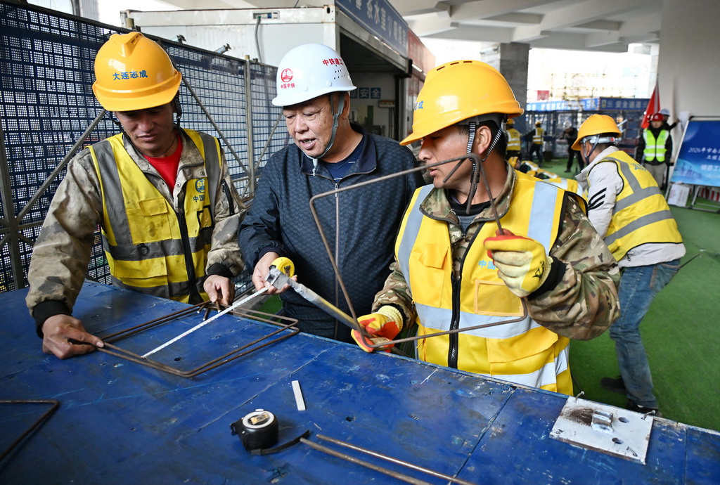 4月8日，在青岛市南京路1号项目比赛现场，一名评委（左二）在钢筋工团体赛中测量钢筋。