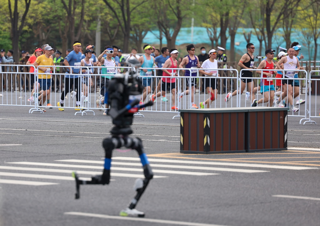 4月19日，参赛的长跑选手与杭U赛队自主人形机器人选手宇树H1（前）在比赛中。新华社记者 翟一凡 摄