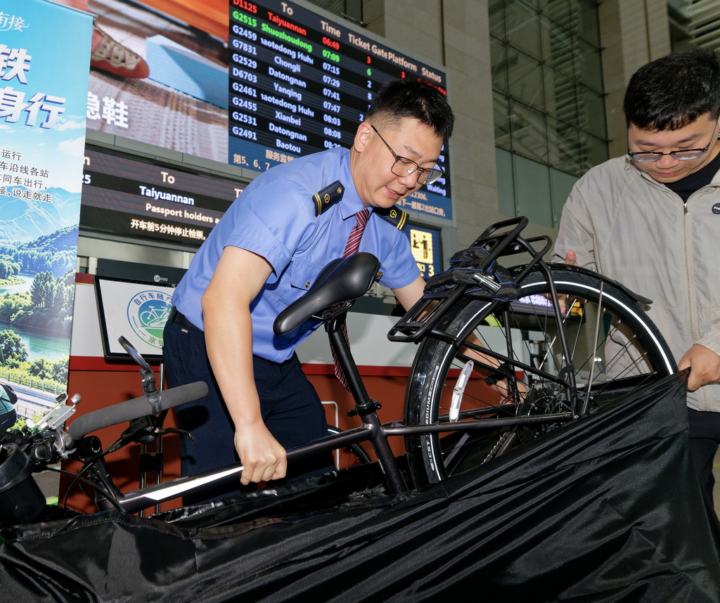 5月19日，工作人员在北京北站检票口处协助将随行自行车放入车站提供的免费装车袋。新华社记者 张笑宇 摄