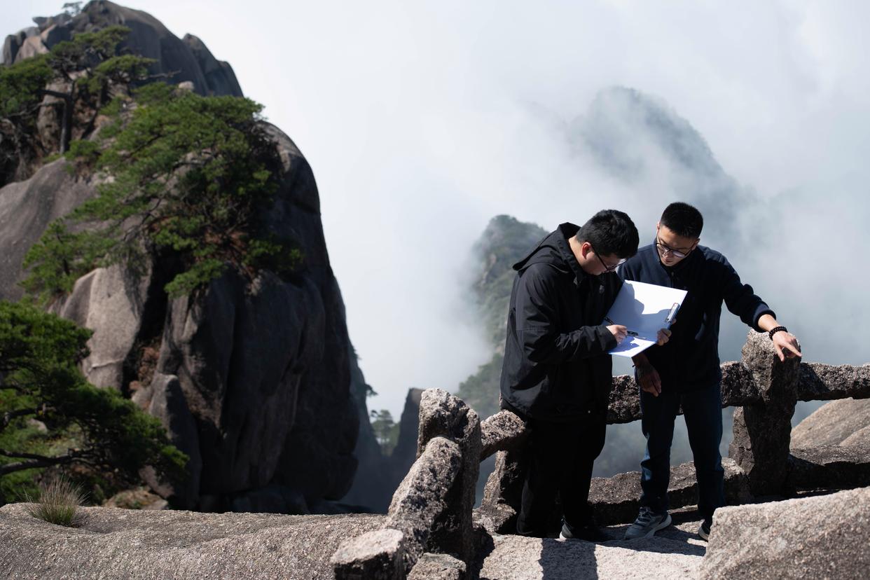 2025年4月23日，黄山风景区文化事业管理办公室副主任俞杨阳（右）与同事盛泽洋在封闭轮休中的莲花峰记录沿途石刻文物信息。新华社记者 张端 摄